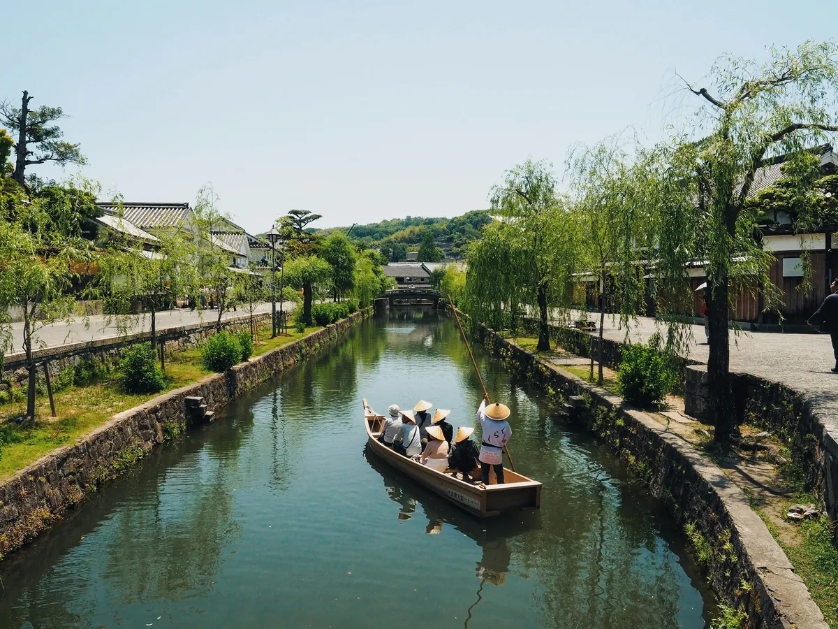 Traditional boat with passengers gliding along the canal of the Bikan quarter among willows, in Kurashiki