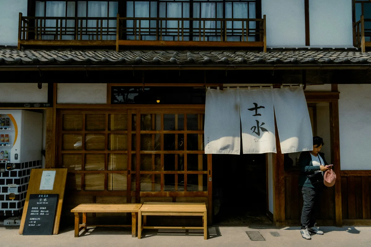 Traditional wooden facade and white wall with a hanging noren, on a street of the Bikan quarter in Kurashiki