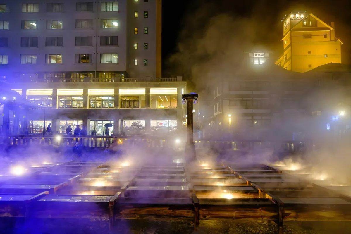 Illuminated wooden channels of the Yubatake with steam in Kusatsu at night