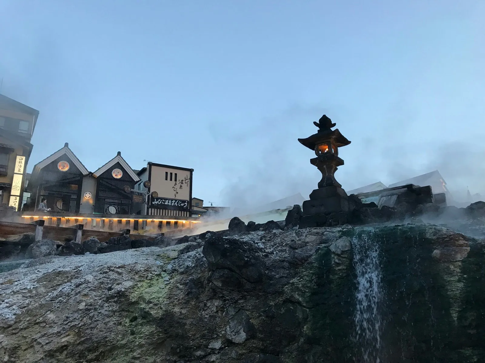 Steaming Yubatake hot-spring field with a stone lantern in Kusatsu Onsen